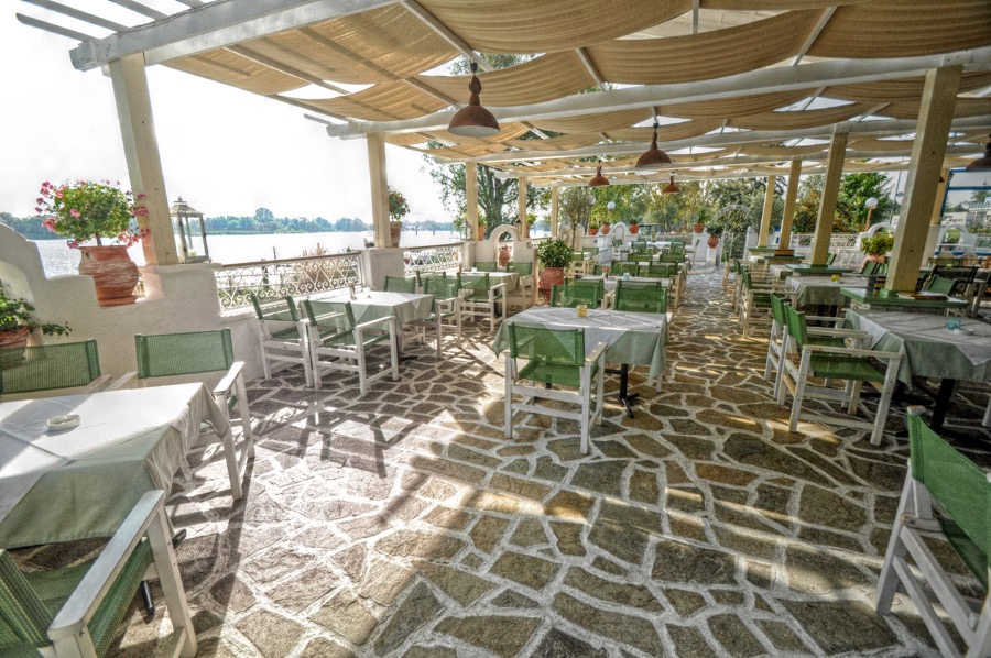 Sonnige Mesogios-Terrasse mit gedeckten Tischen, mediterranen Pflanzen und Blick auf die Havel